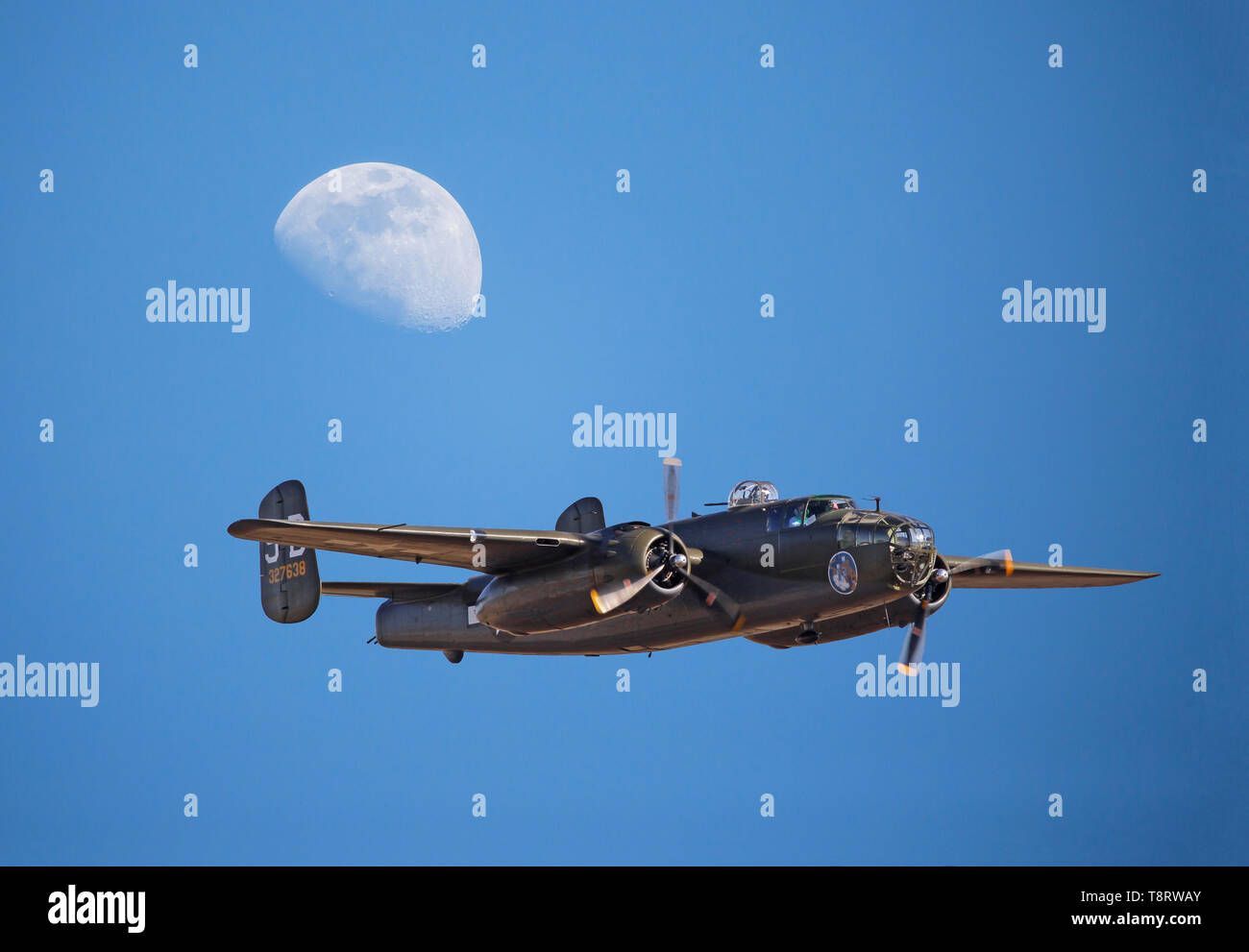 Ein vintage Weltkrieg II B-25 Mitchell Bomber fliegt unter einem gibbous Mond in einem tiefblauen Himmel. Stockfoto