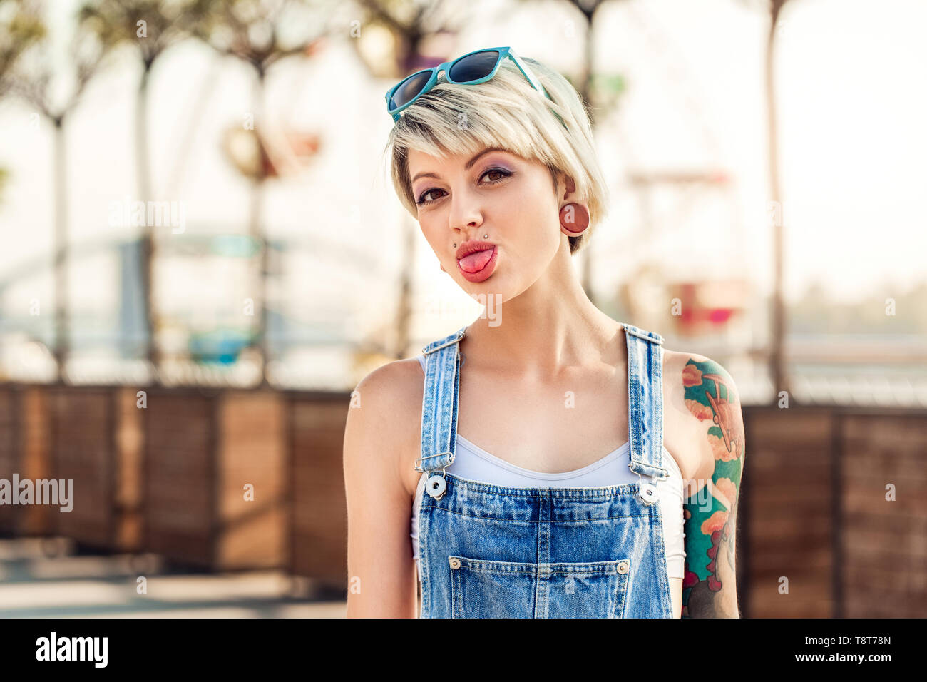 Junge alternative Mädchen mit Sonnenbrille auf dem Kopf stehend auf die Stadt Straße Kamera zeigt Zunge verspielten close-up Stockfoto