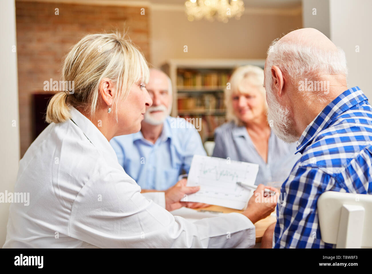 Weibliche Arzt schaut nach Senioren in einer Therapiesitzung und zeigt ihm ein Diagramm Stockfoto
