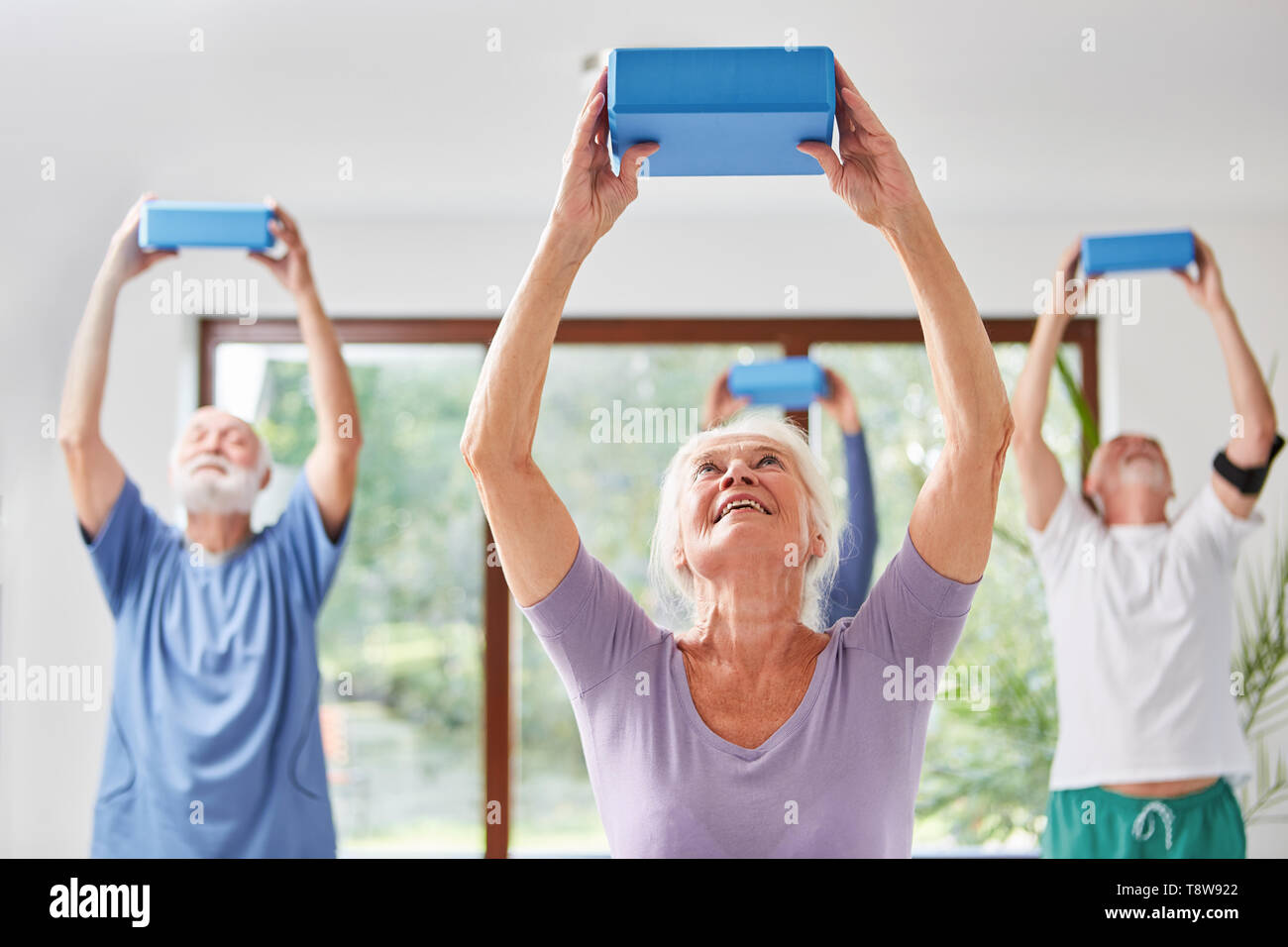 Vitale Senioren zurück Training mit Yoga Block in einem rehabilitationskurs Stockfoto