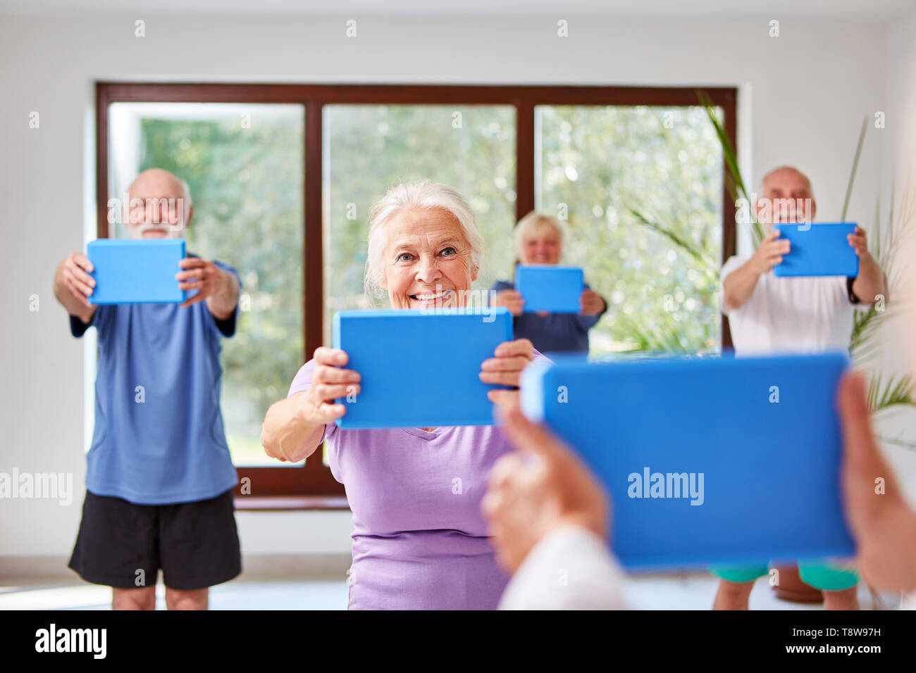 Ältere an eine rehab zurück Übung mit dem Yoga Block in der Turnhalle Stockfoto