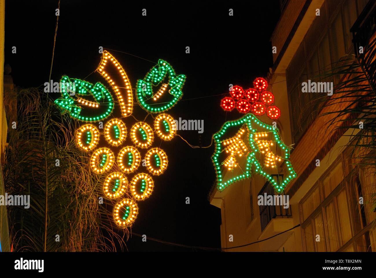 Holly und Trauben Weihnachten Licht Dekoration auf der anderen Straßenseite in der Nacht ausgesetzt, Fuengirola, Costa del Sol, Provinz Malaga, Andalusien, Spanien, Europa. Stockfoto