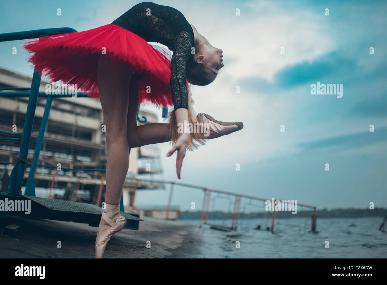 Ballerina tanzt an der Küste des Flusses in einem schwarzen und roten Tutu gegen den Hintergrund der Gebäude. Stockfoto