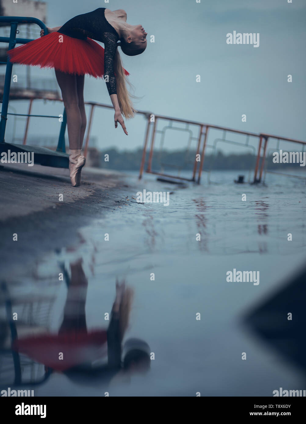 Ballerina tanzen an der Küste des Flusses in einem schwarzen und roten Tutu und ihr Spiegelbild im Wasser. Stockfoto