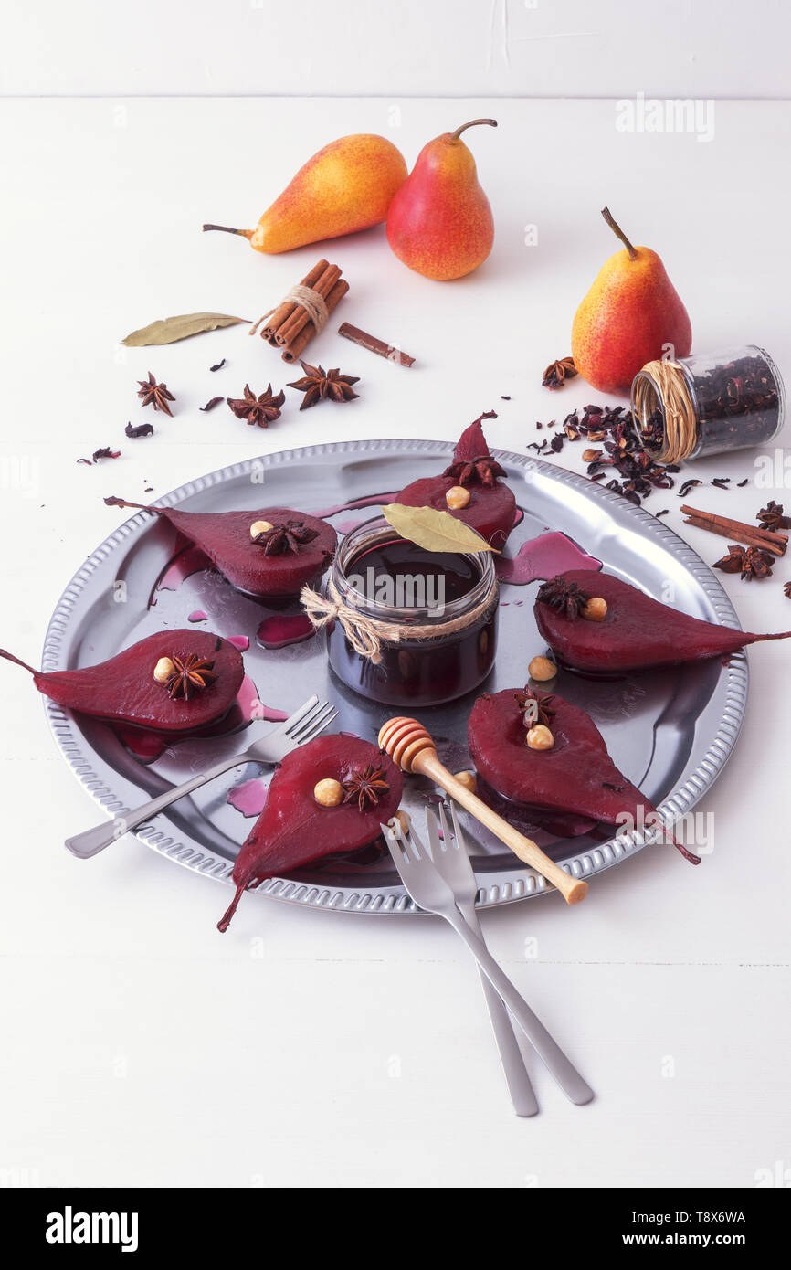 Hibiscus pochierte Birnen, süße Frucht Dessert. Silber Tablett mit Birnen, mit Haselnüssen, Lorbeerblätter verschönert, getrocknet Hibiskusblüten, Anis Sterne, und Stockfoto