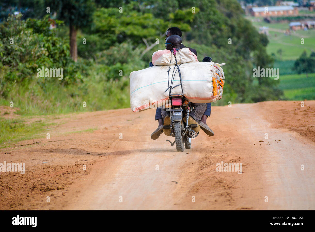 Zwei Männer auf einem Motorrad zusammen mit grosse Säcke von Waren auf eine unbefestigte Straße nach Dedza Stadt Malawi Stockfoto