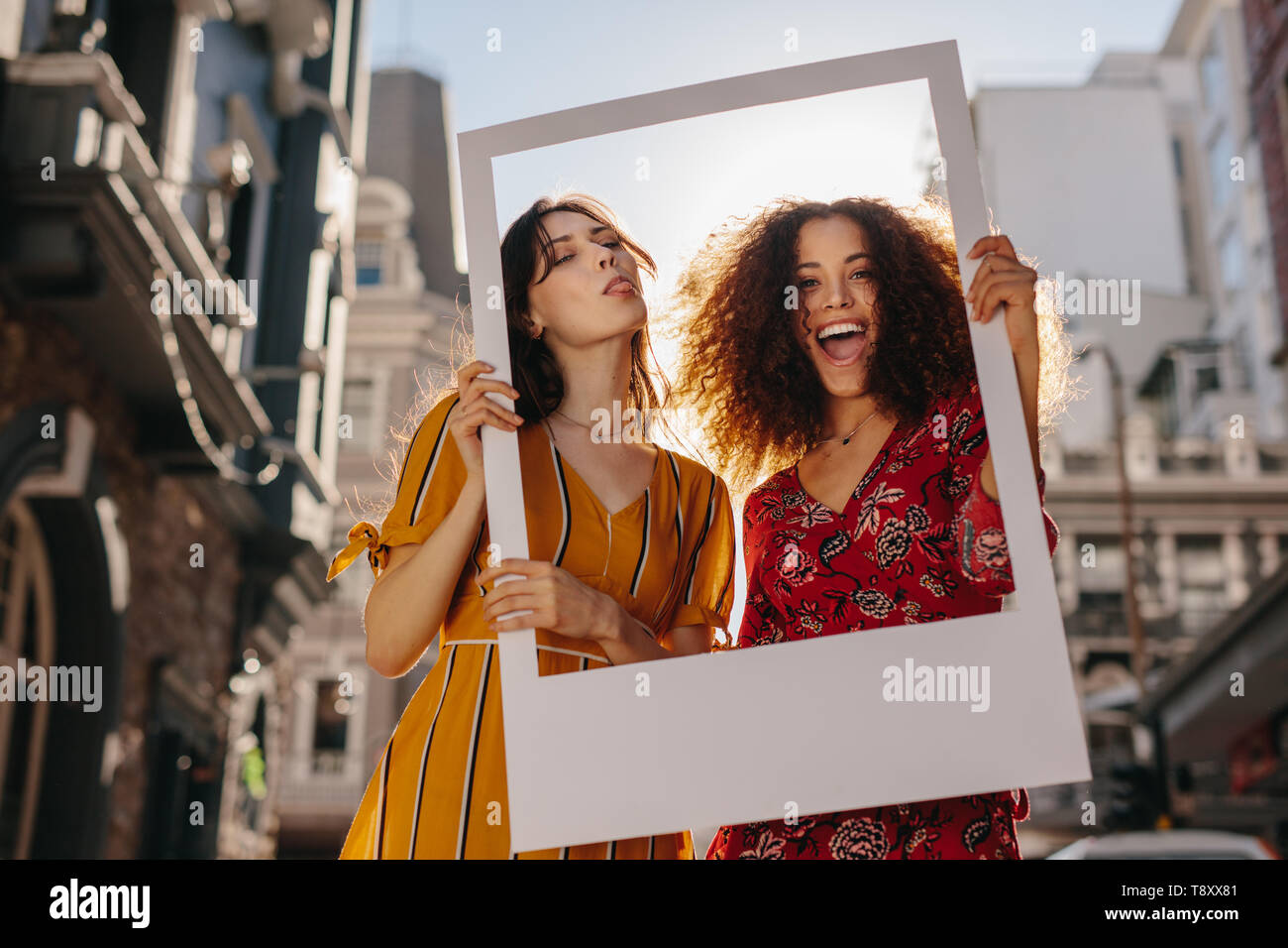 Schöne Frauen, die sich in einem leeren Fotorahmen in Front. Attraktive Frauen mit einem leeren Bilderrahmen an Kamera schauen, Lachen und die Zunge Stockfoto