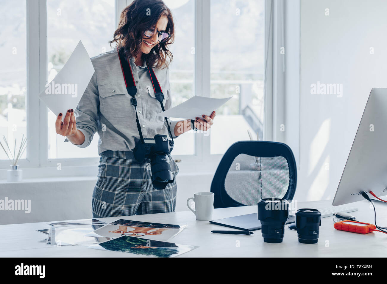 Junge Frau mit einer DSLR-Kamera um den Hals, der an ihrem Schreibtisch und der Auswahl der besten Bilder von fotoshooting. Fotografin am p suchen Stockfoto