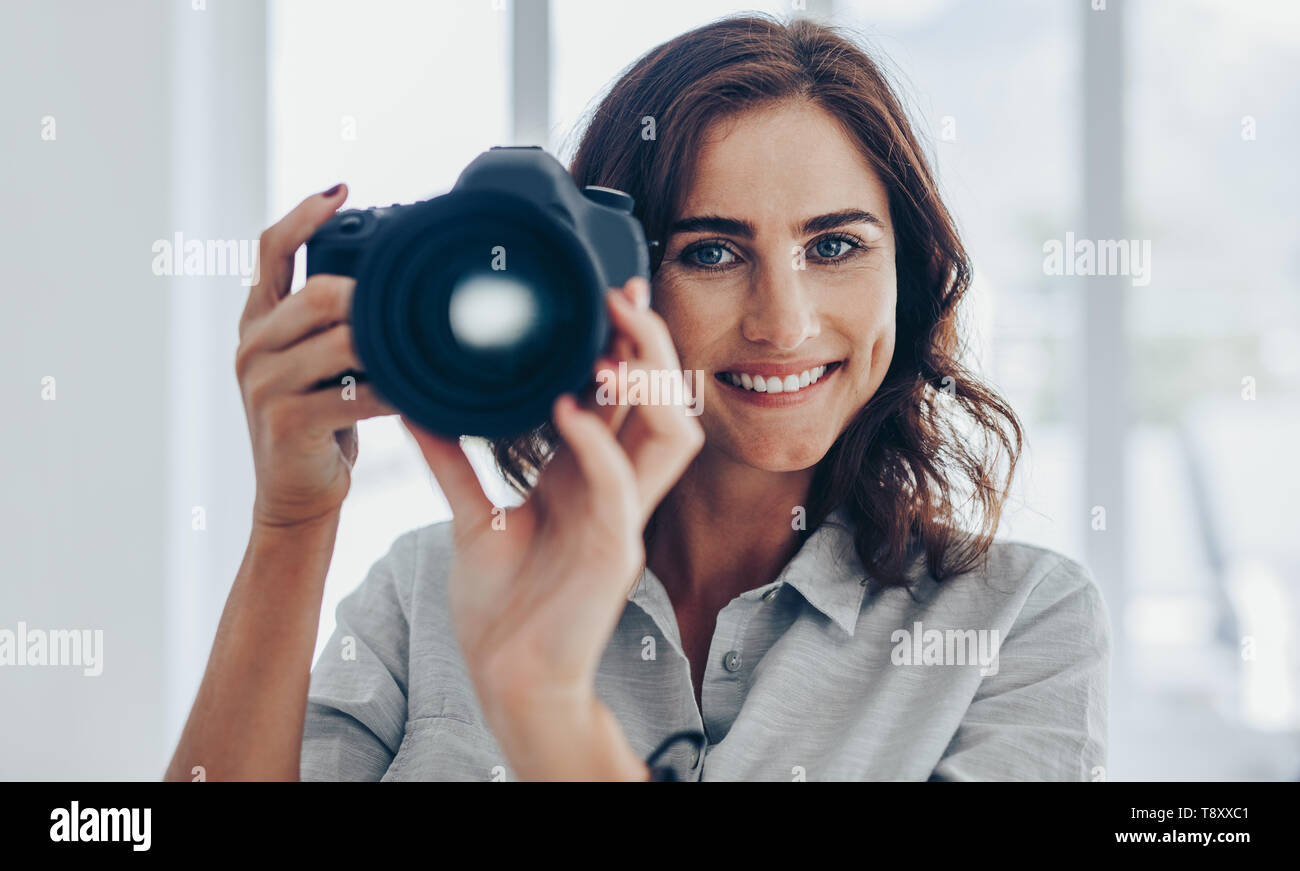 Schöne junge Fotografin mit DSLR-Kamera fotografieren. Glückliche Frau schiessen mit einer professionellen Kamera. Stockfoto