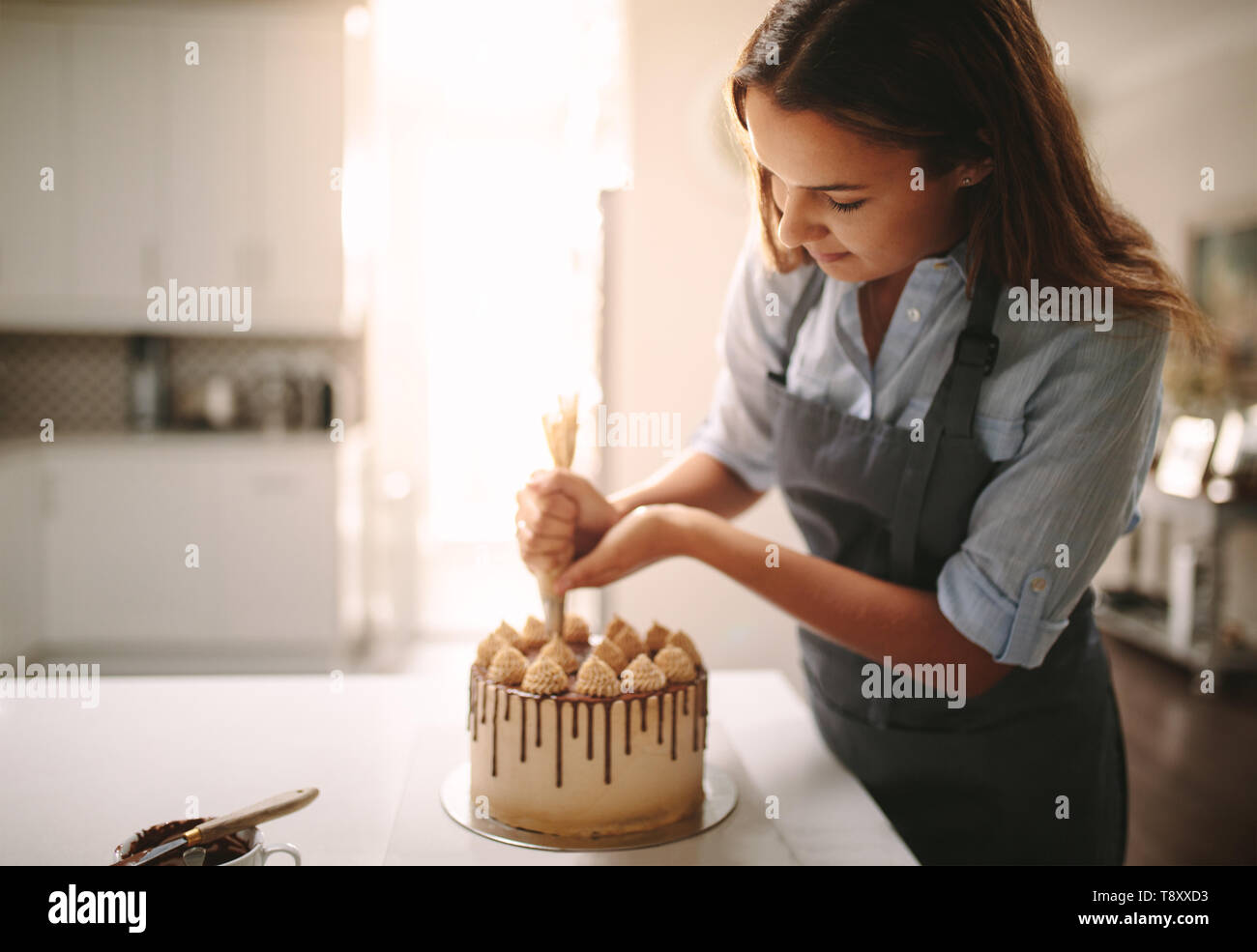 Frau verzieren Schokolade Kuchen in der Küche. Frau Koch, einen Kuchen zu Hause. Stockfoto