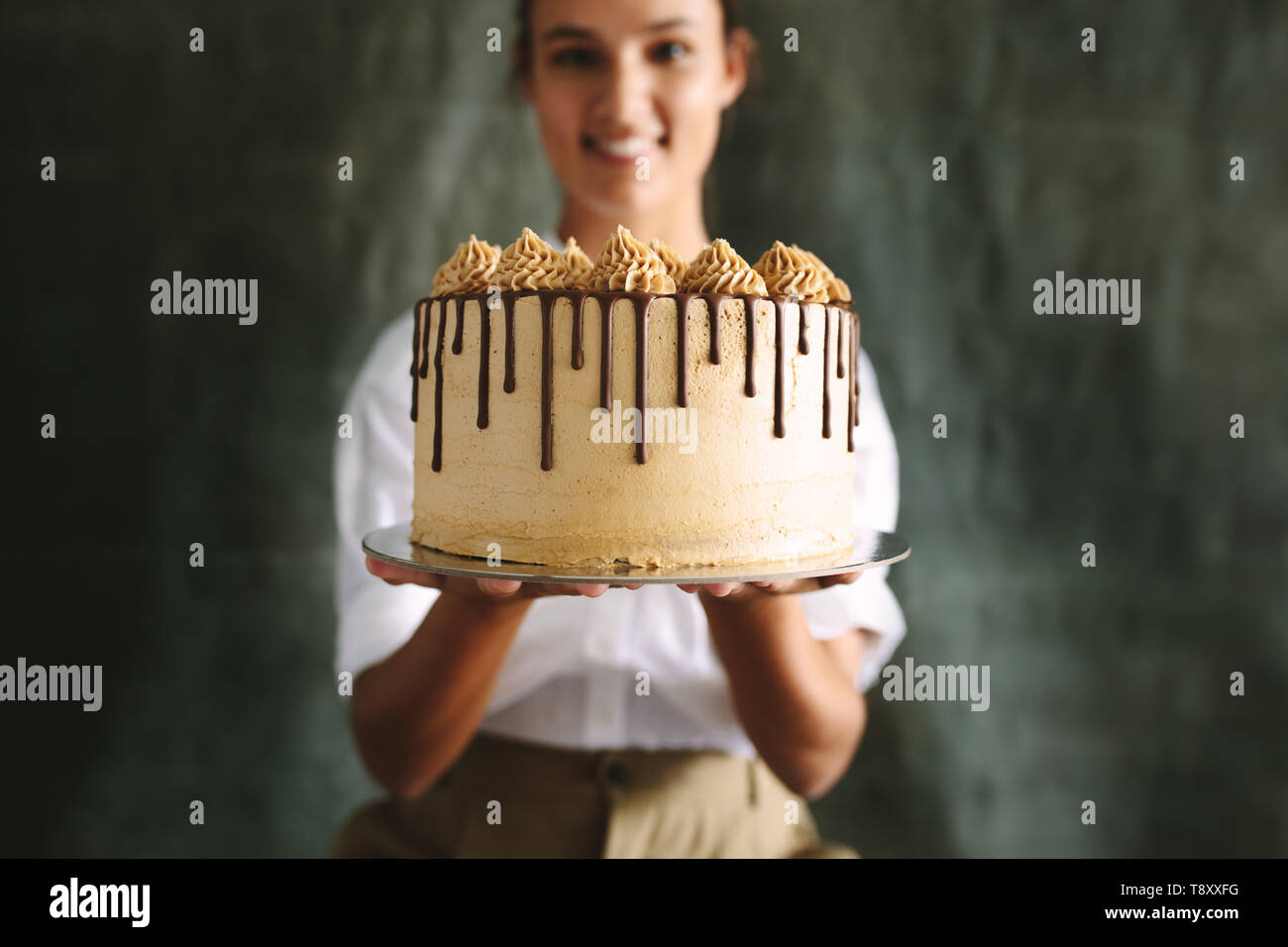 Weibliche baker Holding einen leckeren Kuchen. Koch Holding frisch gebackenen Kuchen gegen grauen Hintergrund. Stockfoto