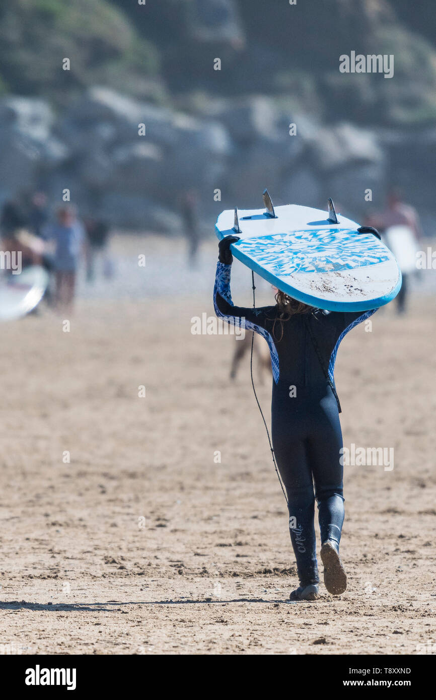 Ein junger Surfer mit einem Surfbrett auf dem Kopf und von dort über den Fistral Beach in Newquay in Cornwall. Stockfoto