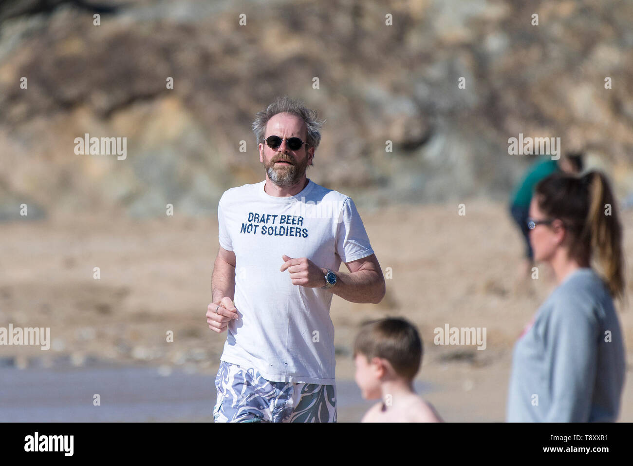 Ein reifer Mann, der ein T-Shirt mit einem lustigen Slogan Joggen entlang der Küste auf den Fistral Beach in Newquay in Cornwall. Stockfoto