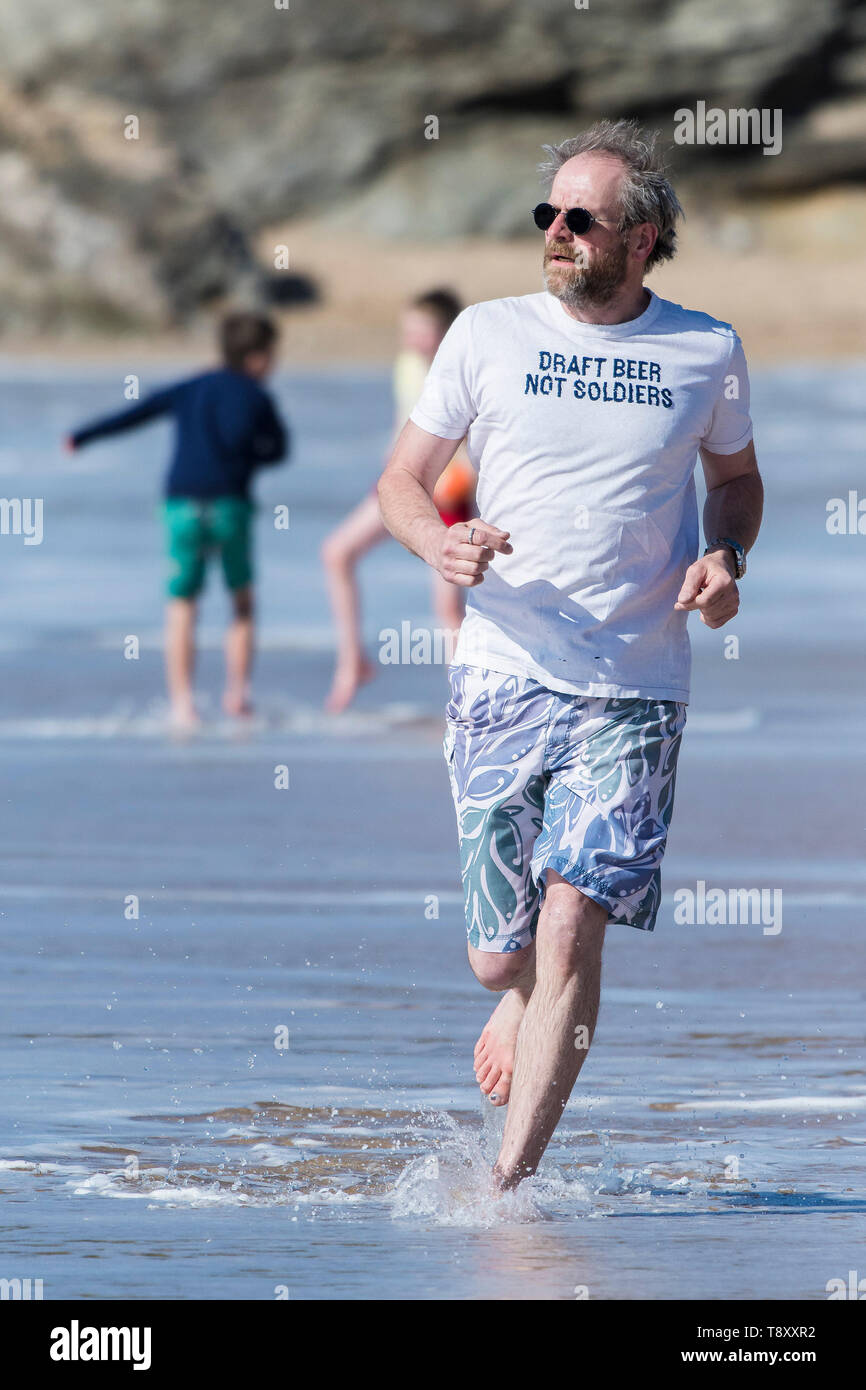 Ein reifer Mann, der ein T-Shirt mit einem lustigen Slogan Joggen entlang der Küste auf den Fistral Beach in Newquay in Cornwall. Stockfoto