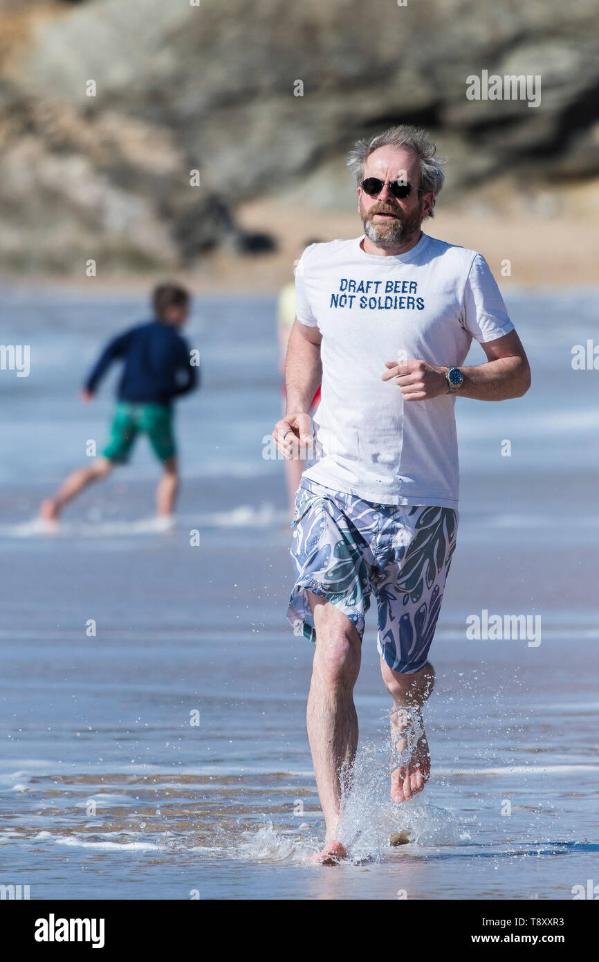 Ein reifer Mann, der ein T-Shirt mit einem lustigen Slogan Joggen entlang der Küste auf den Fistral Beach in Newquay in Cornwall. Stockfoto