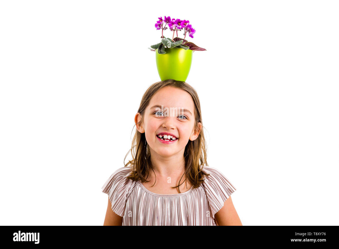 Mädchen mit Blumentopf auf den Kopf, Spaß haben ein Lächeln auf den Lippen. Kleines Mädchen im Kleid holding Green Flower Pot mit Viola Blumen auf dem Kopf Spaß, vermasseln Stockfoto