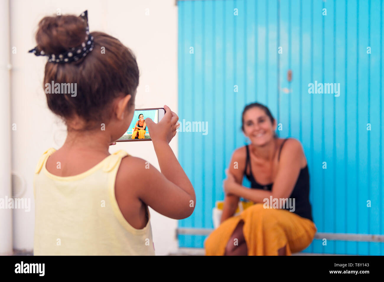 Kleines Mädchen nimmt Fotos mit dem Smart Phone zu ihrer Mutter vor einem blauen Tür, Ein-eltern-Familie auf Urlaub, geschiedene Frau mit Er Stockfoto
