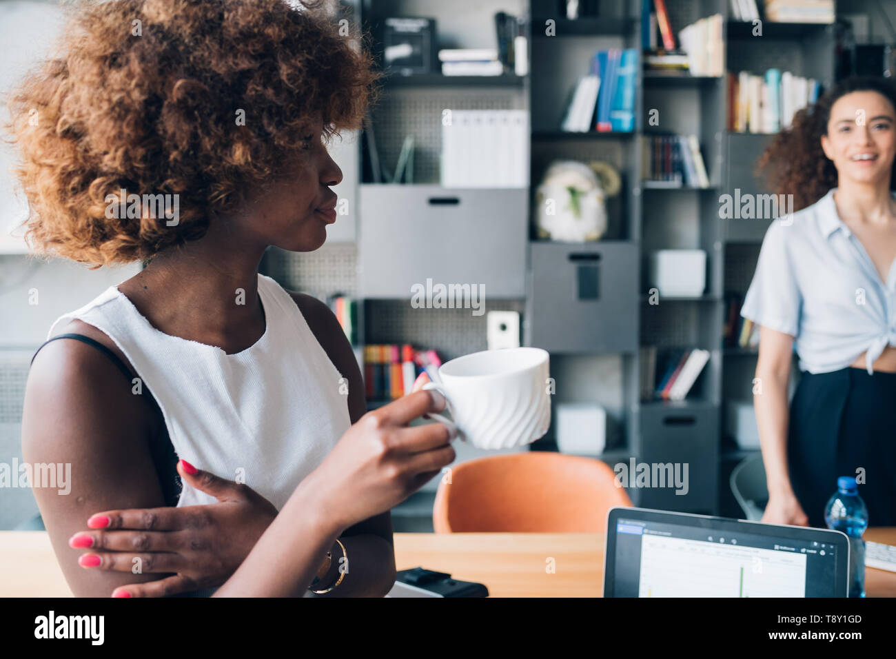 Junge schwarze Frau trinkt Kaffee mit Freund in modernen Büro - Planung, Inspiration, findige Stockfoto