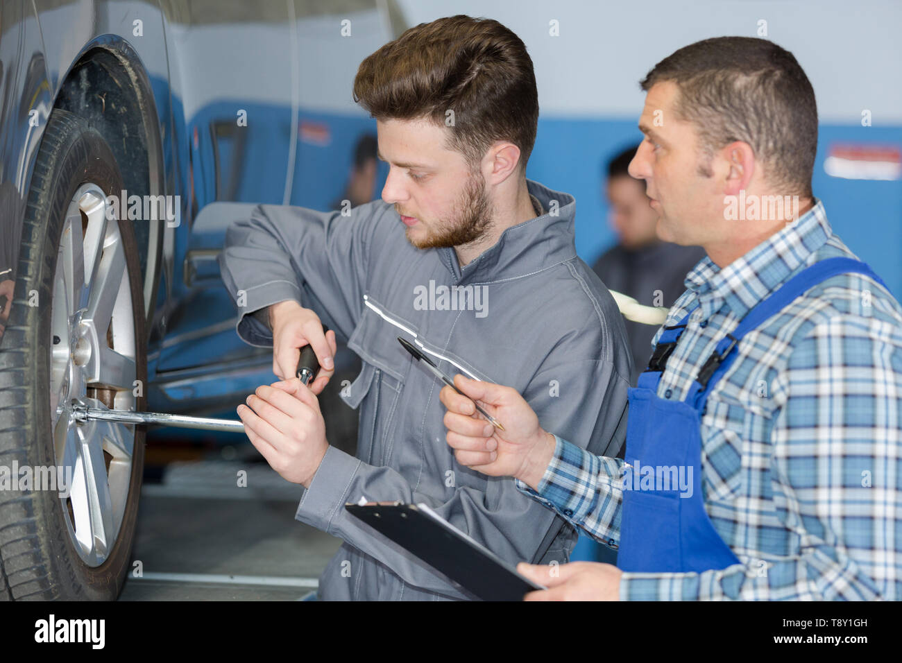 Auszubildende lernen, Reifen in einer Garage ändern Stockfoto