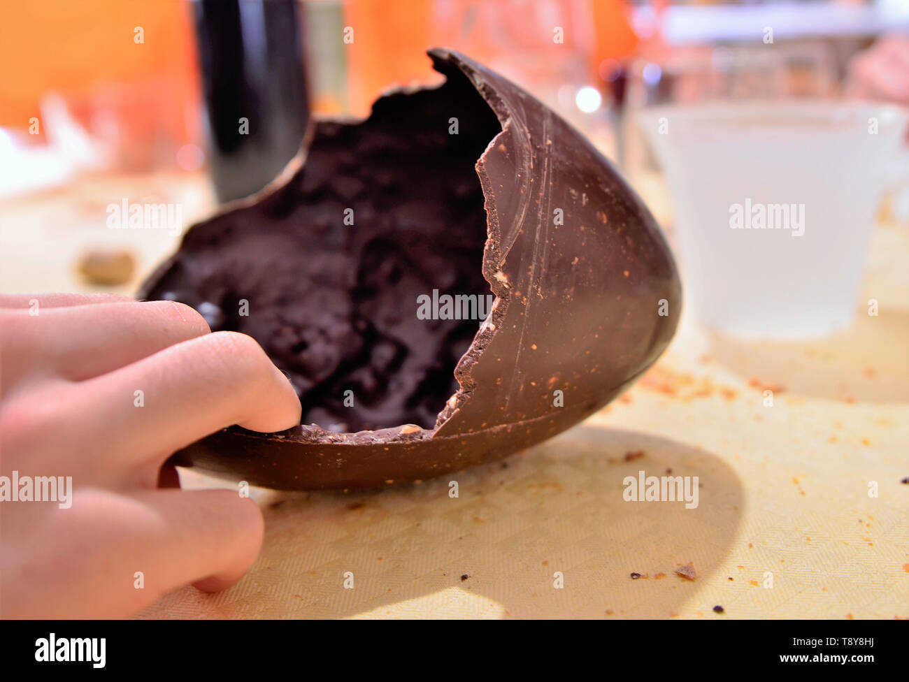 Ein Osterei wurde geöffnet, die zerbrochene Schokolade shell ist auf die Tabelle in Ihrer Verpackung ruht. Die Hand eines kaukasischen Mann schneidet ein Stück Nahrung. 30. Stockfoto