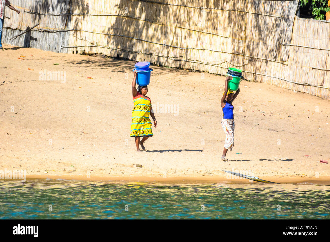 Zwei junge MALAWISCHE Frauen mit Eimer auf dem Kopf kommen zum Lake Malawi um Wasser zu zeichnen Stockfoto