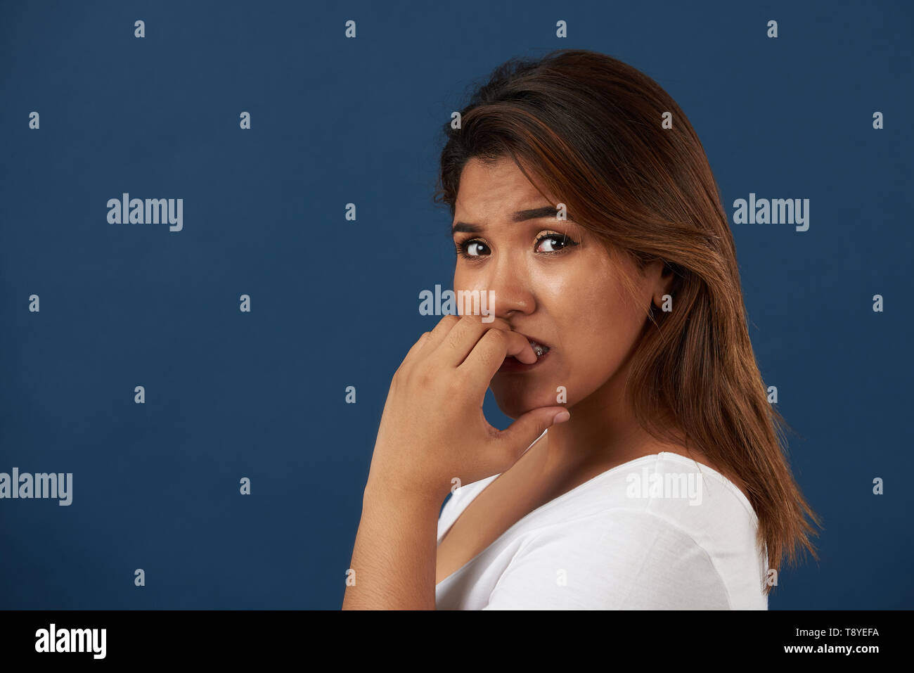 Junge Frau essen ihre Nägel Portrait auf blauem Hintergrund isoliert Stockfoto