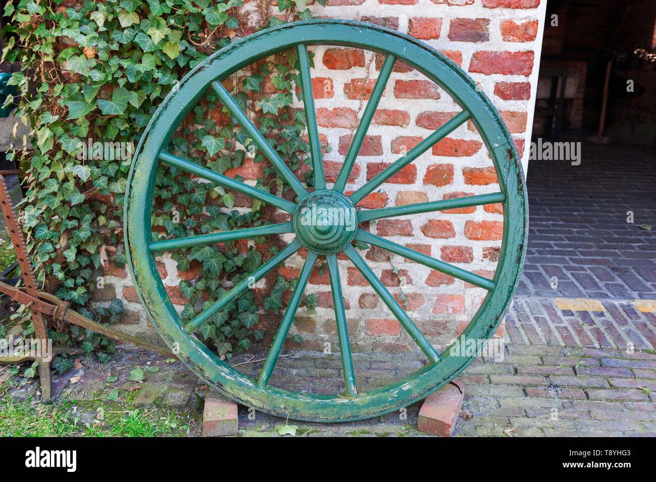 Altes Pferd Warenkorb Rad mit grünen abblätternden Lack Beschichtung gegen einen Ziegel Wand lehnt. Stockfoto