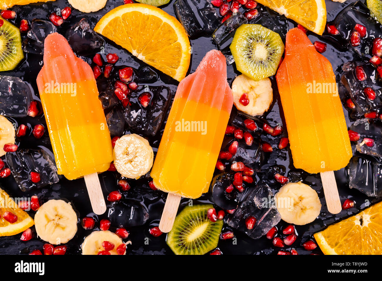 Obst Eis auf Stick mit Scheiben Früchte auf schwarzem Schiefer. Fokus auf Eis am Stiel. Stockfoto
