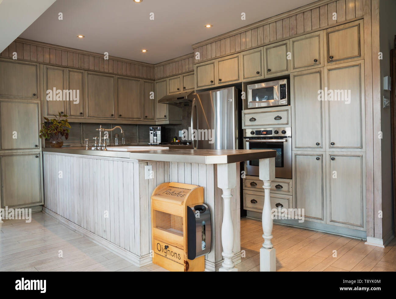 Küche im Landhausstil mit grau faux finish Schränke, Keramik Arbeitsplatte  und Plank Holz Imitation Vinyl Bodenbelag innerhalb eines alten 1820  Landhausstil fieldstone Haus mit gestapelten log Erweiterung, Quebec,  Kanada. Dieses Bild ist