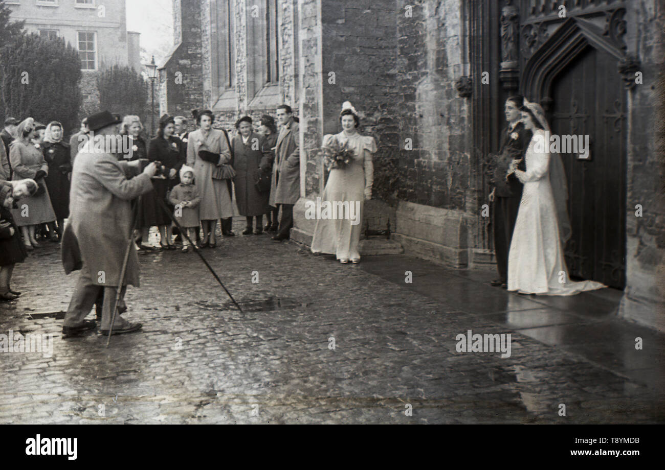 1950, historische, eine frisch verheiratete Ehepaar vor der Tür einer Kirche in ihr Bild von der Hochzeit Fotografen, mit seiner Kamera auf einem Stativ, England, UK. Stockfoto