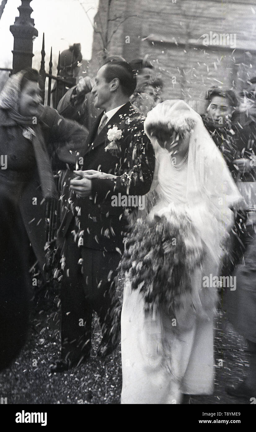 1950 s, historischen, nach der Hochzeit Service, sehen wir eine Braut und Bräutigam geduscht oder mit Konfetti durch die Gäste vor den Toren der Kirche geworfen, England, UK. Stockfoto