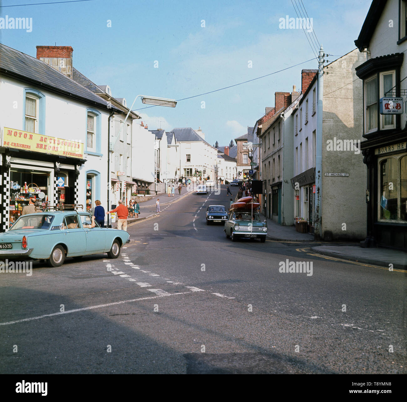 1960, historische Bild aus dieser Ära der St. Michael Straße, Brecon, Powys, Wales, in dem die Kammern Family Motor Parts Shop und ganz rechts, der M&B Boars Head Pub. Stockfoto