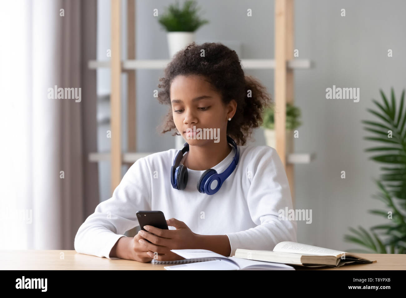 Afrikanische amerikanische jugendlich Mädchen mit Telefon, von Hausaufgaben ablenken Stockfoto