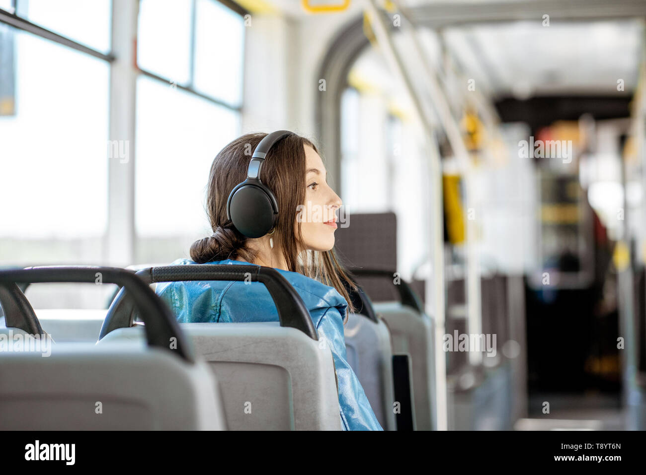 Junge Frau Passagier genießen Urlaub im öffentlichen Verkehr, sitzend mit Kopfhörern in der modernen Straßenbahn. Ansicht von hinten Stockfoto