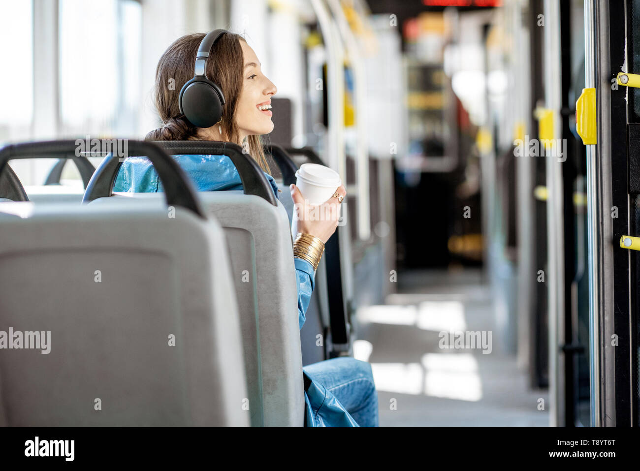 Junge Frau Passagier genießen Reise an die öffentlichen Verkehrsmittel, mit Kopfhörern und Kaffee in der modernen Straßenbahn sitzen. Ansicht von hinten Stockfoto