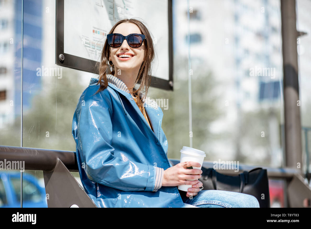 Junge stilvolle Frau wartet auf den öffentlichen Verkehr und die Moderne tram station draußen sitzen Stockfoto
