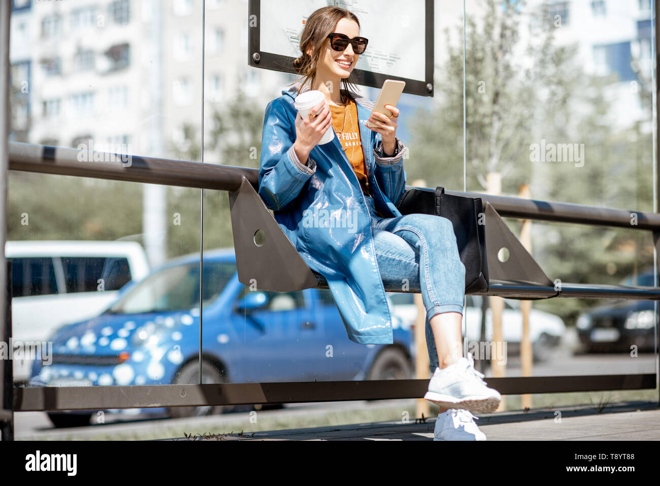 Junge stilvolle Frau wartet auf den öffentlichen Verkehr und die Moderne tram station draußen sitzen Stockfoto
