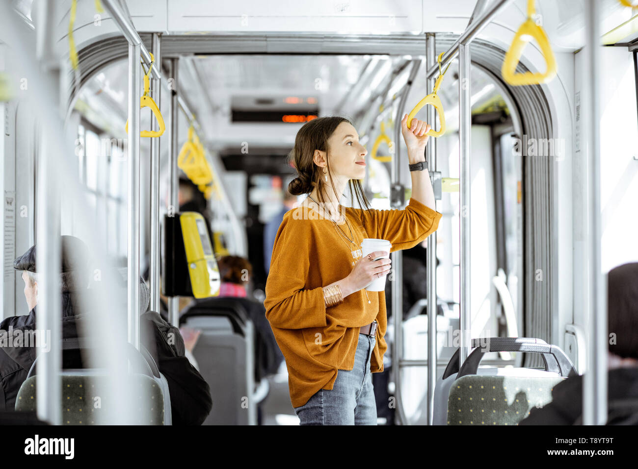 Junge Frau Passagier genießen Reise an die öffentlichen Verkehrsmittel, mit Kaffee in der modernen Straßenbahn stehend Stockfoto