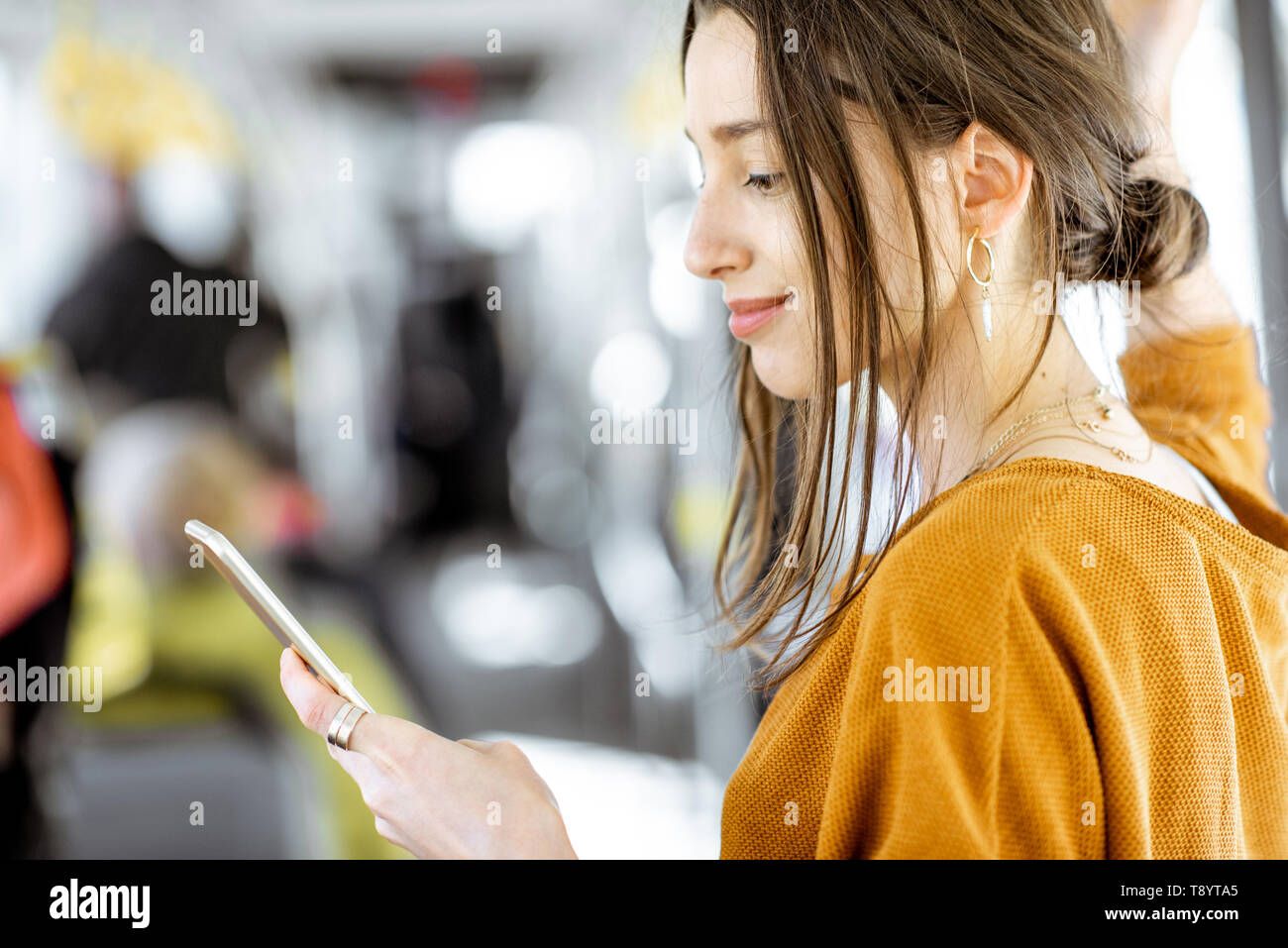 Nahaufnahme Porträt einer jungen Frau mit Smartphone, während in der modernen Straßenbahn stehend Stockfoto