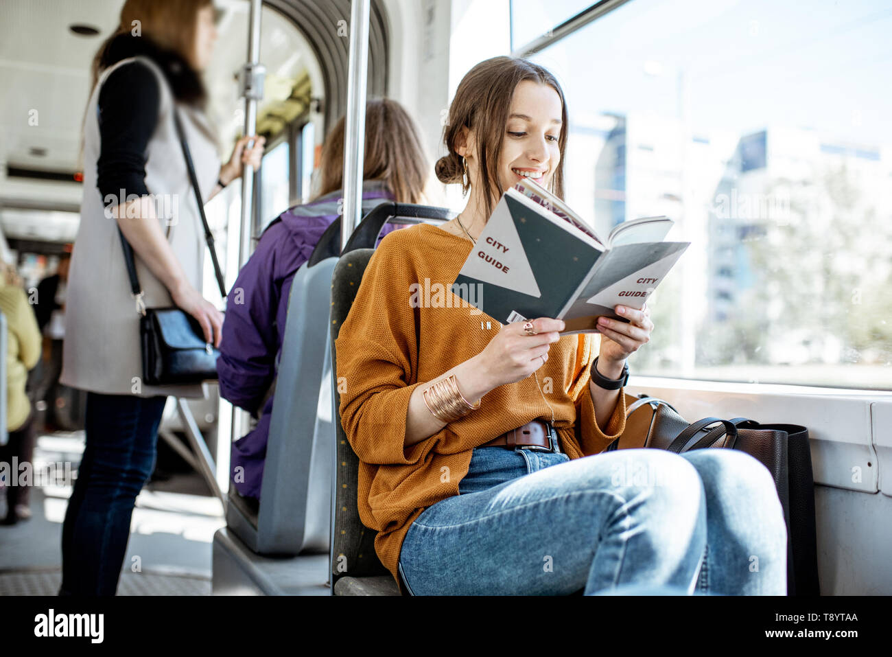 Junge Frau mit Buch beim Bewegen in der modernen Straßenbahn, glücklich Passagier an der öffentlichen Verkehrsmittel Stockfoto