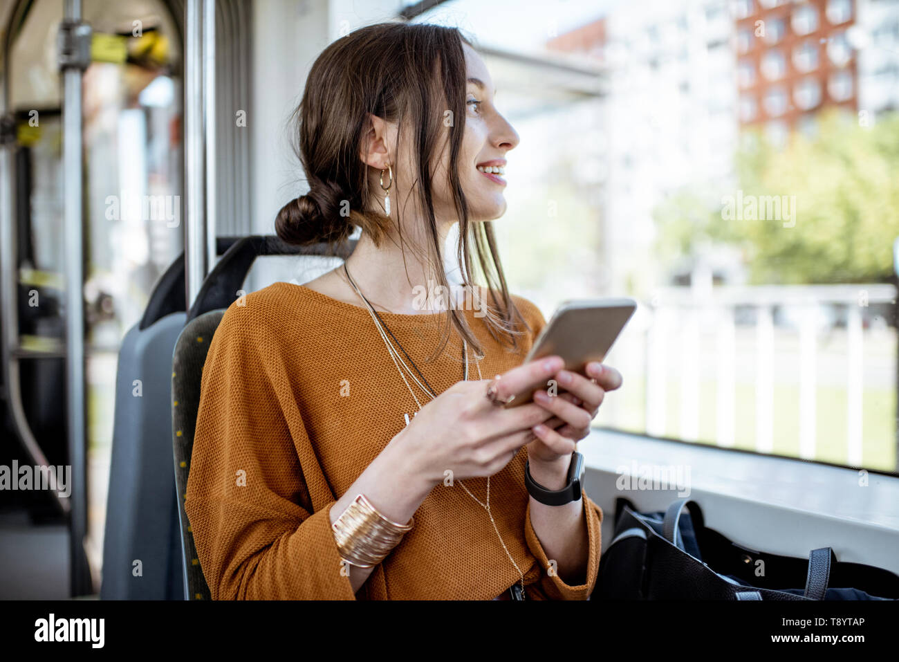 Junge und glückliche Frau mit Smartphone, während in der Nähe der Fenster in den öffentlichen Verkehrsmitteln sitzen während der Fahrt Stockfoto