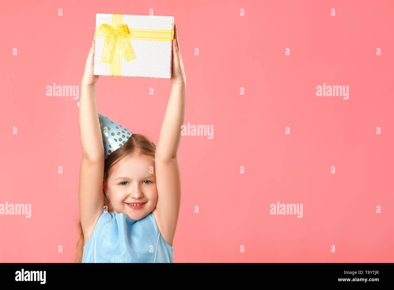 Ein fröhliches kleines Mädchen in einem Gap hält eine Box mit einem Geschenk über ihrem Kopf. Porträt eines Kindes auf einem rosa Koralle Hintergrund. Kopieren Sie Platz. Stockfoto