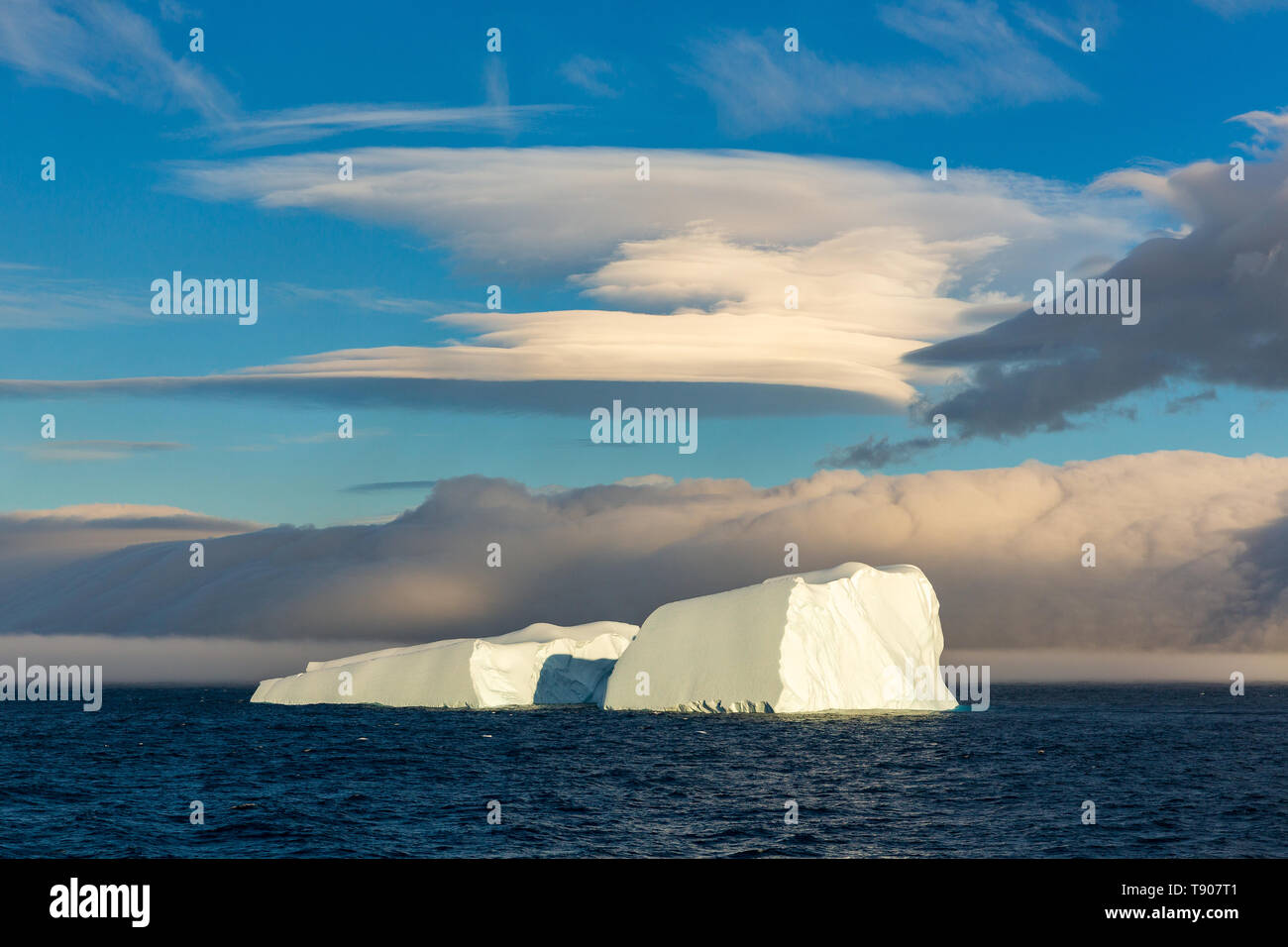 Eine spektakuläre eckig Eisberg aufgeteilt in zwei Hälften schwimmt unter einem Linsenförmigen Wolke von Elephant Island im Südlichen Ozean Stockfoto