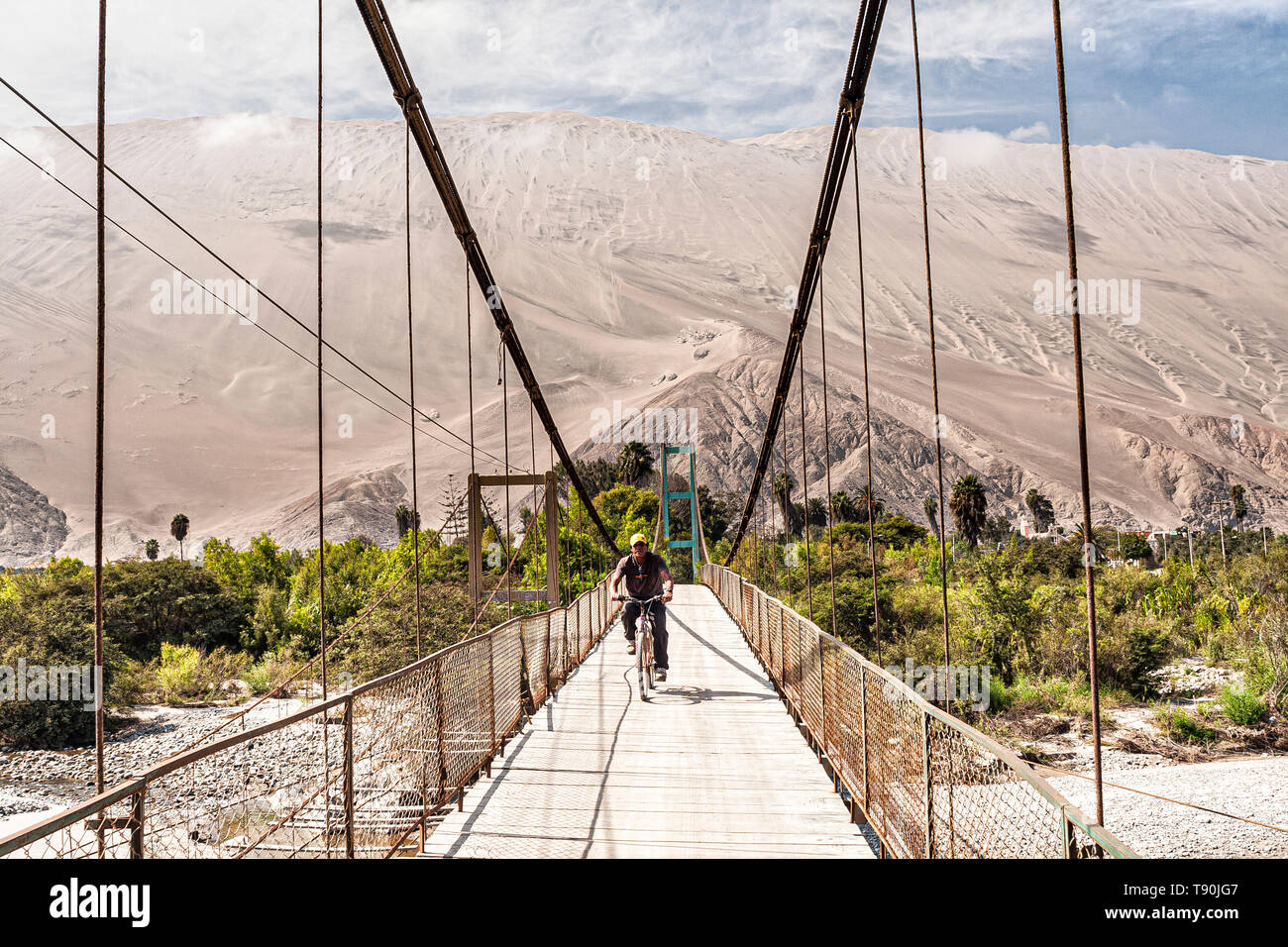 Mann mit dem Fahrrad auf der Fußgängerbrücke über Acari Fluss und Cerro Toro Mata im Hintergrund. Acari, Abteilung von Arequipa, Peru. Stockfoto