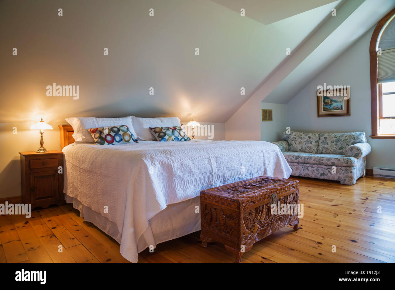 King size Bett mit geschnitzten exotische Holz- Brust und gepolstertes Sofa  im Schlafzimmer mit Pinienwald Dielen auf der oberen Etage in einem 90er  Jahre zeitgenössische im Viktorianischen Stil, Country Home, Quebec, Kanada.