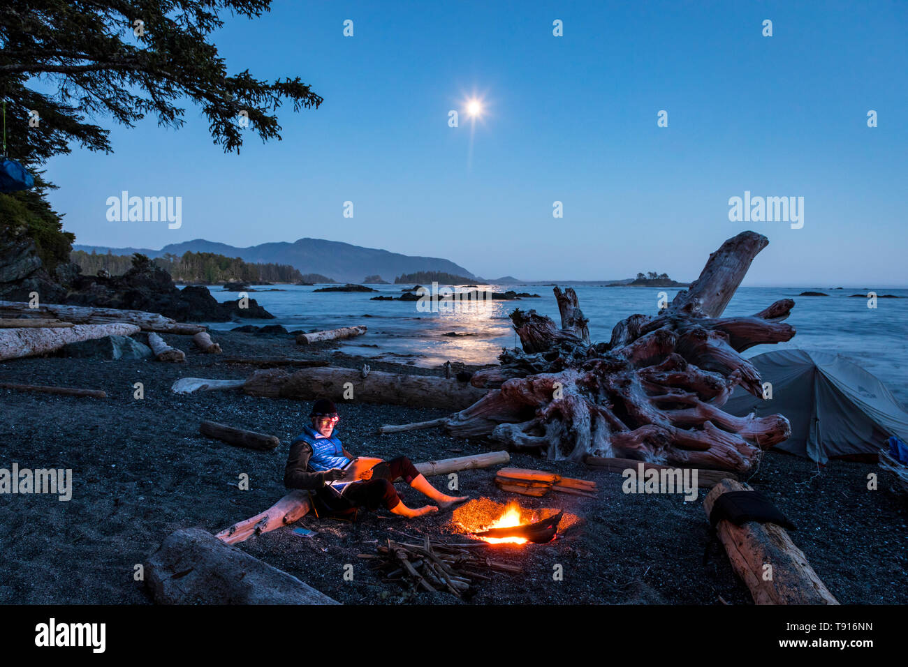 Ein einsamer Camper sitzt am Lagerfeuer auf einer kleinen Insel in Nuchatlitz Provincial Park British Columbia, Kanada Stockfoto