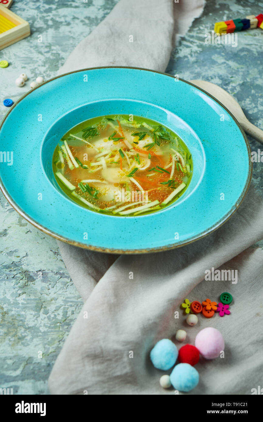 Hühnersuppe mit Grüns in einem blauen Platte. Auf einem grauen strukturierten Hintergrund. Kindermenü. Schöne Servieren von Speisen. Stockfoto