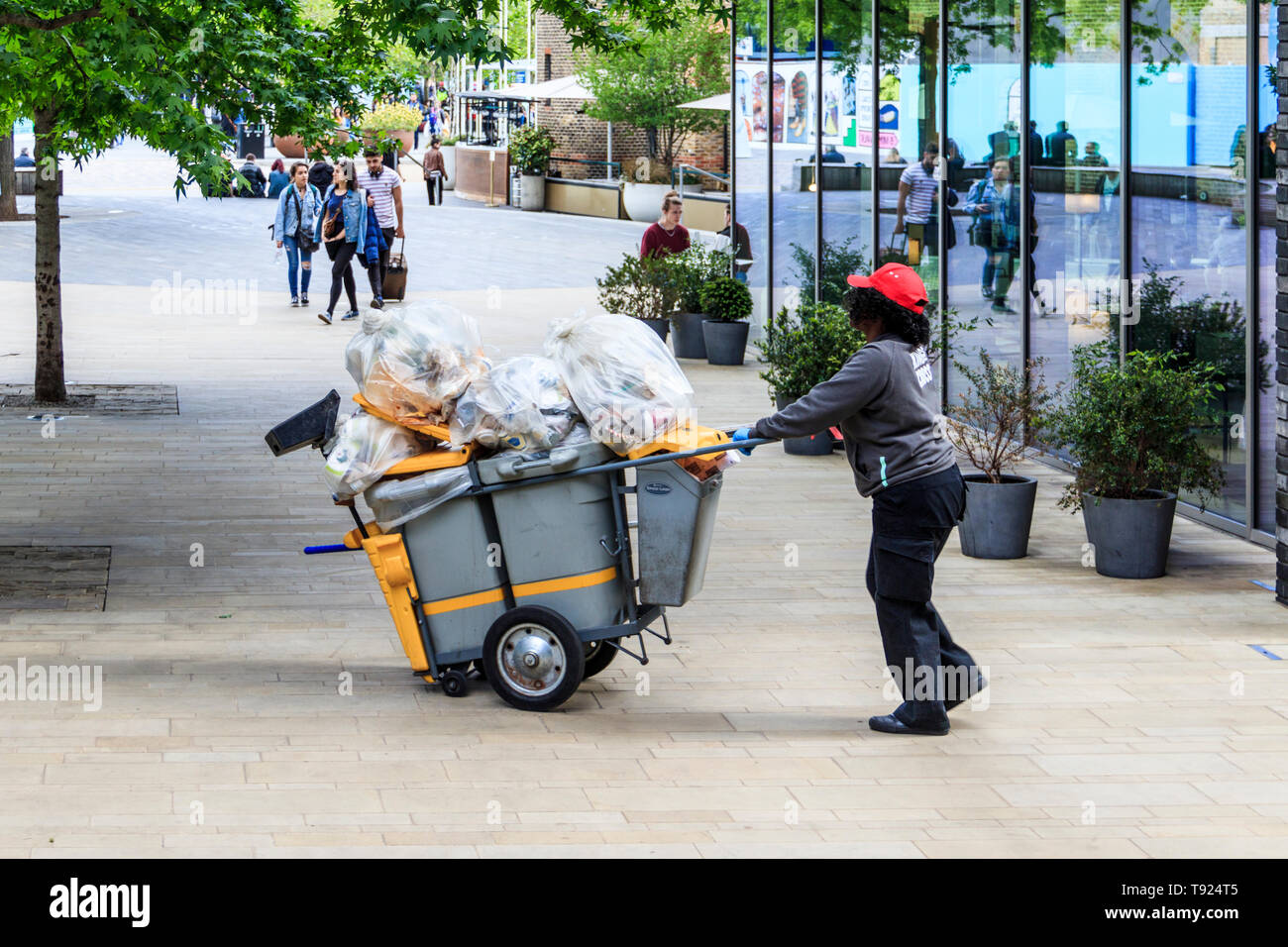 Ein weiblicher Rat street Cleaner drückt ihr Reinigung Transportwagen Pancras Square, King's Cross, London, UK, 2019 Stockfoto