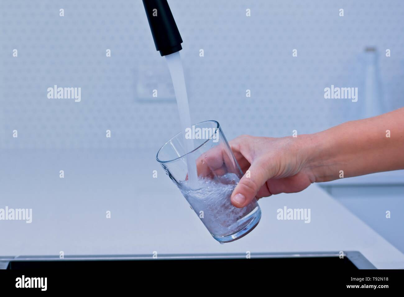 Füllen Sie ein Glas mit Wasser aus einer schwarzen Küche tippen. Stockfoto