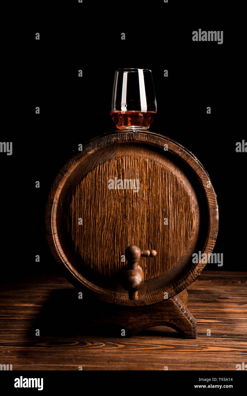 Glas Whiskey auf Holzfass auf schwarzem Hintergrund Stockfoto
